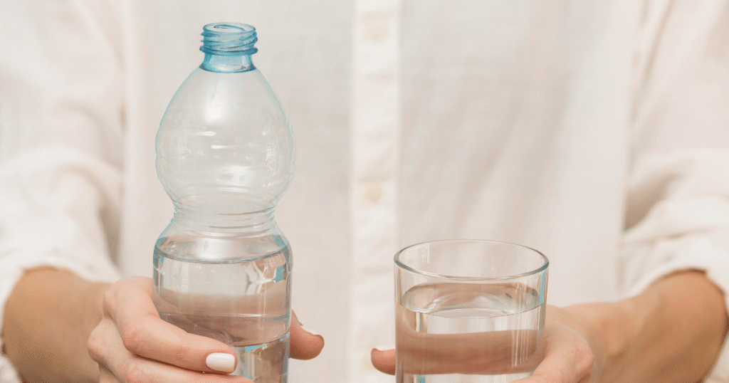 A person holding a bottle of water in one hand and a glass in the other, ready to pour.