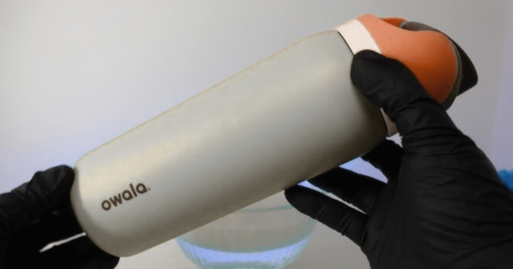 A person holding a plastic Owala bottle with a lid, demonstrating how to clean it effectively.